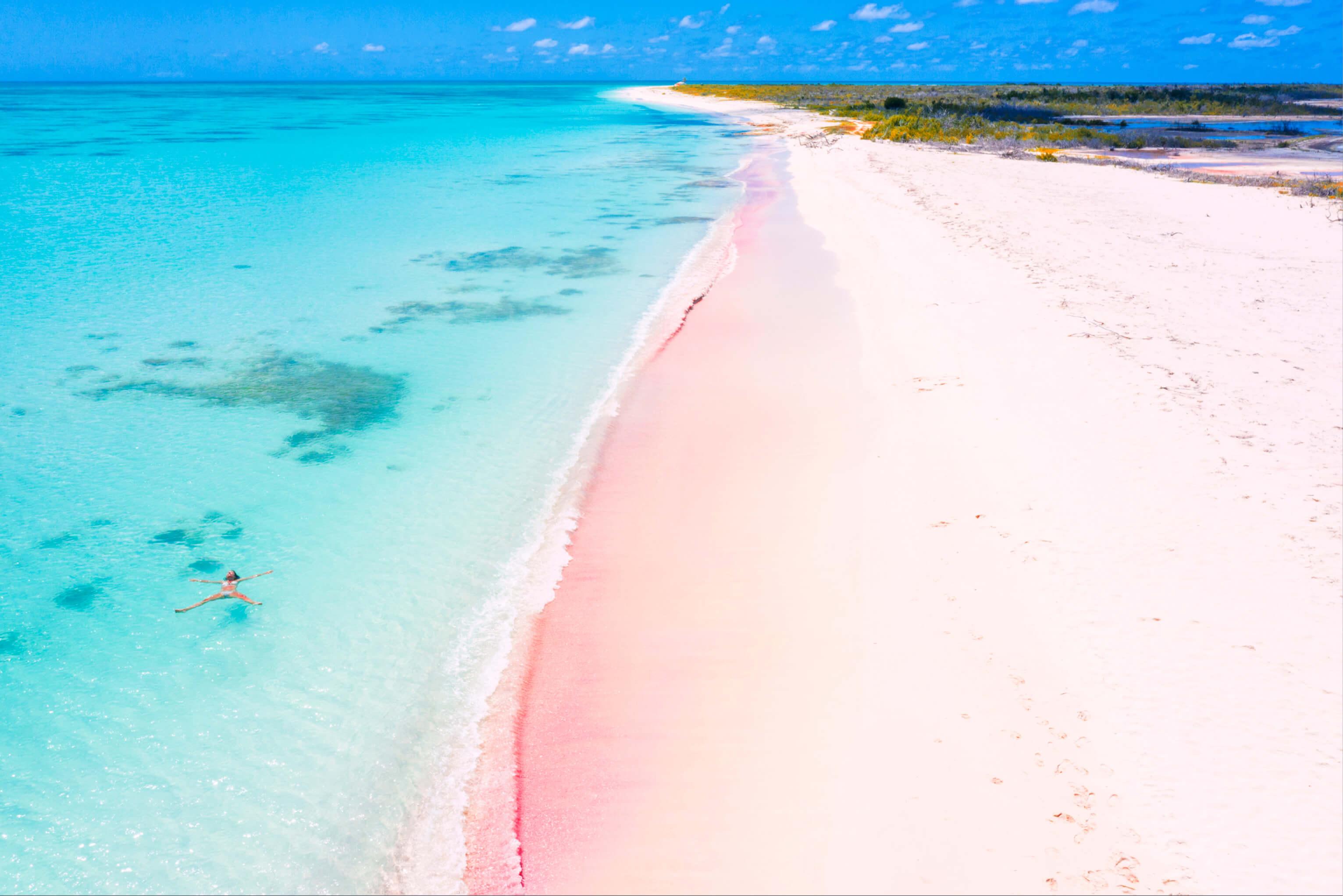A serene beach featuring soft pink sand and clear turquoise water under a bright blue sky