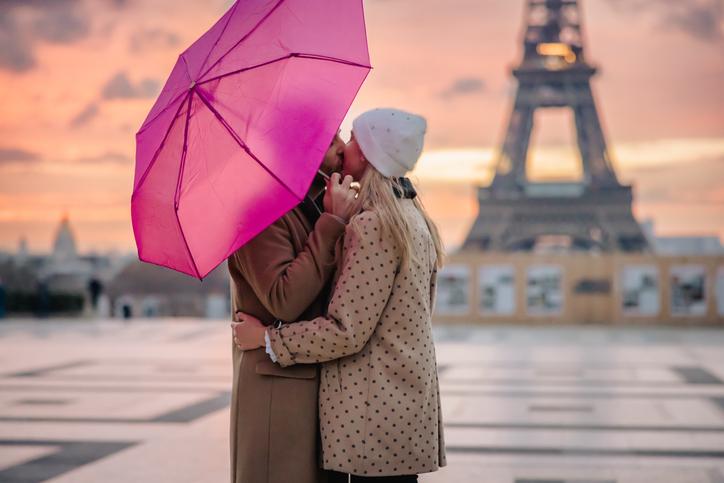 Couple kissing under a pink umbrella with the Eiffel Tower in the background at sunset.