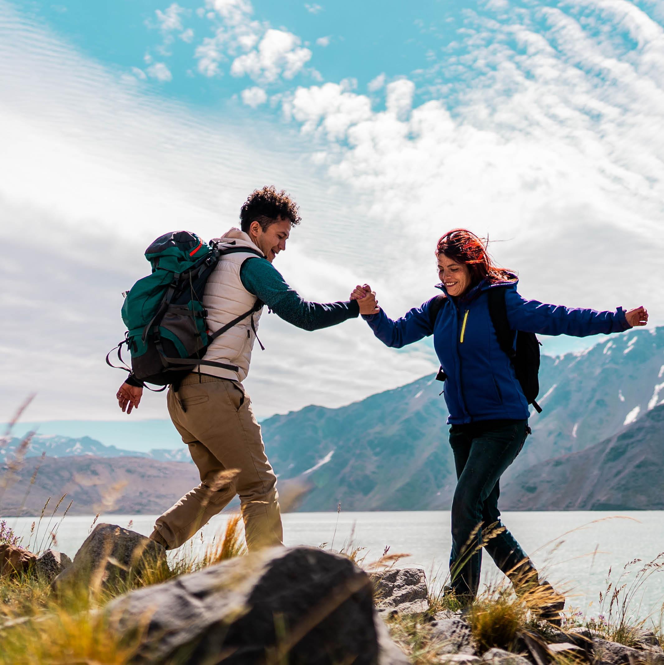 Two hikers clasp hands while climbing over rocks
